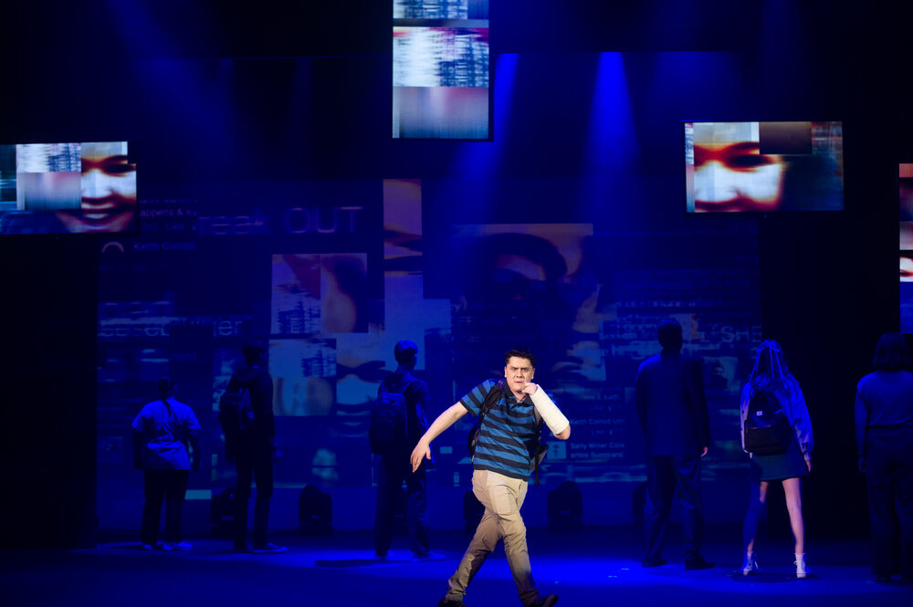 A performer alone downstage, the company in silhouette behind